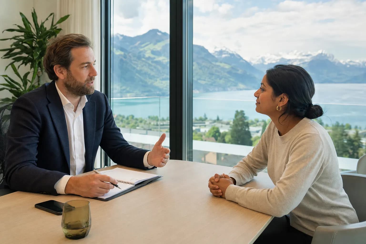 Beraterin und Mandant im Gespräch an einem hellen Besprechungstisch mit Seeblick.